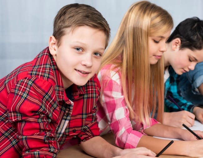Three schoolchildren writing in their exercise books during a group English lesson