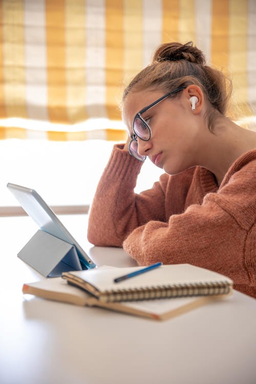 A student with headphones at a tablet and an open exercise book